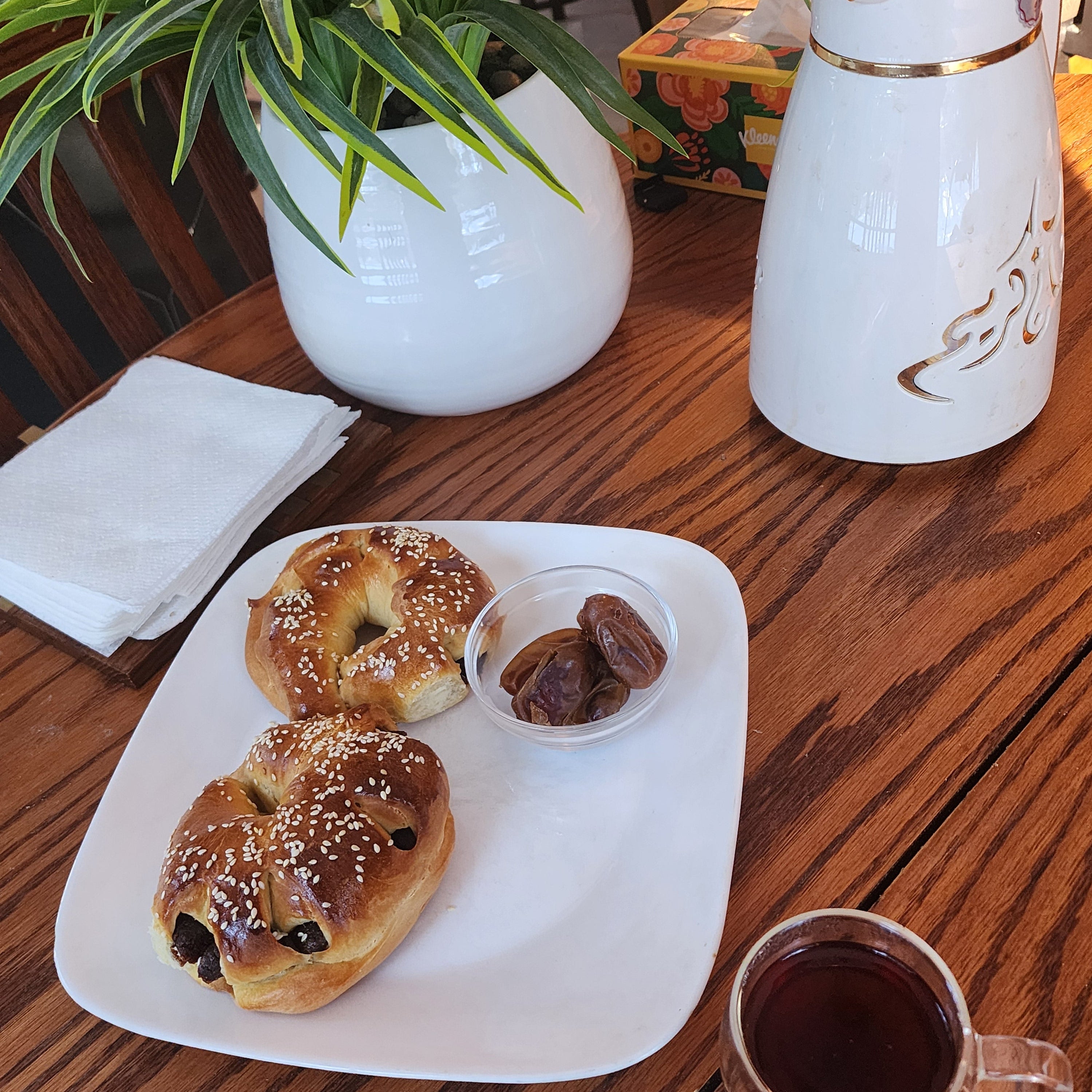 Wooden table with a plate of date breads, a cup of coffee, and decorative items.