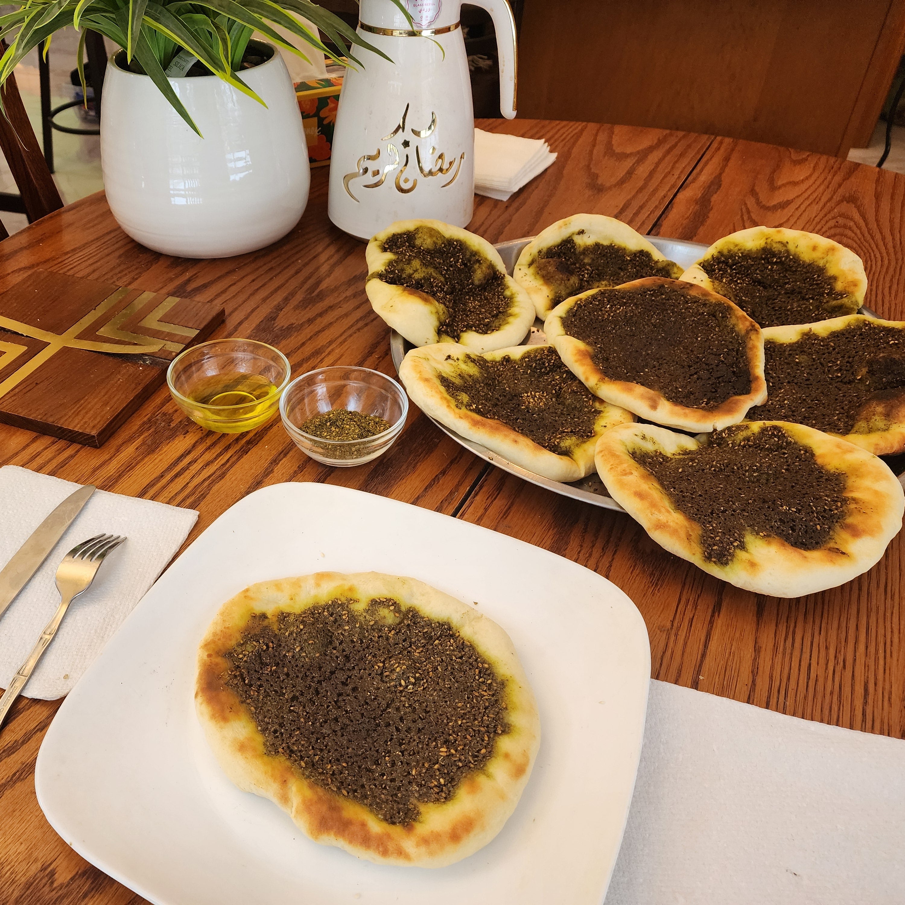 Wooden table with Zaatar pies topped with small bowls, and cutlery.