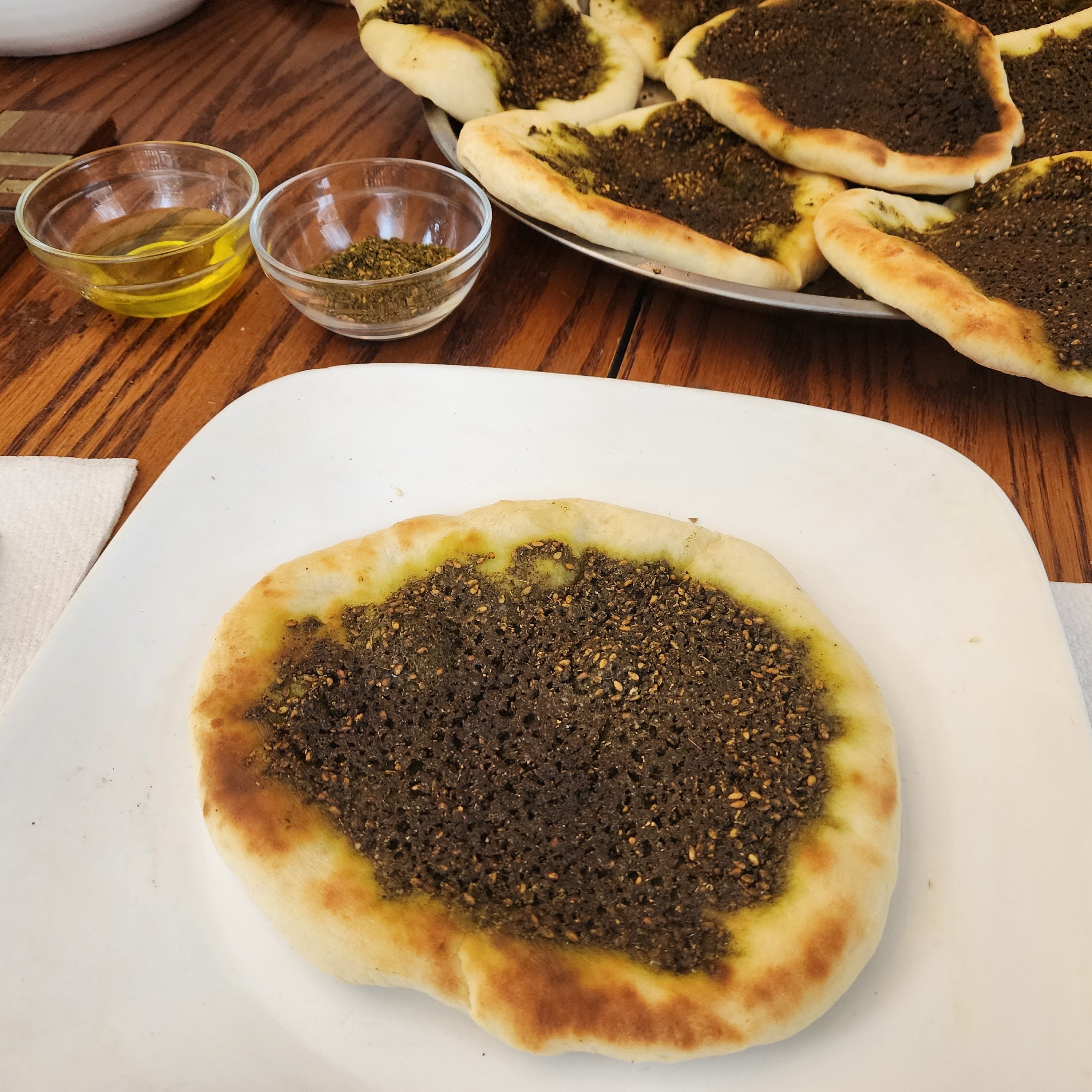 Zaatar Pie on a wooden table with small bowls of oil and herbs.